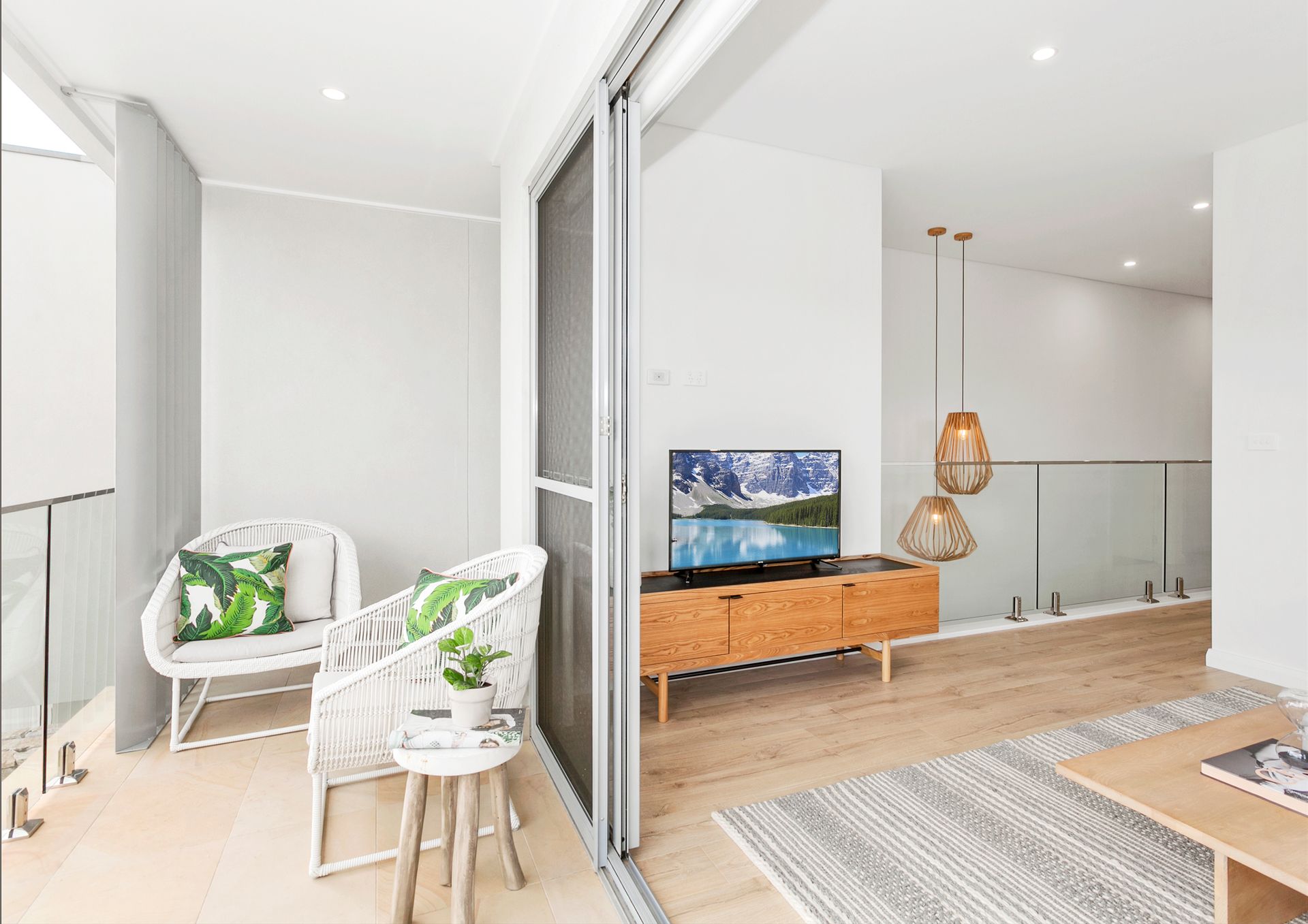 Bright living room with balcony. White walls, wooden floors, and modern furniture. Balcony has chairs and a table — Evolution Building Group In Calderwood, NSW