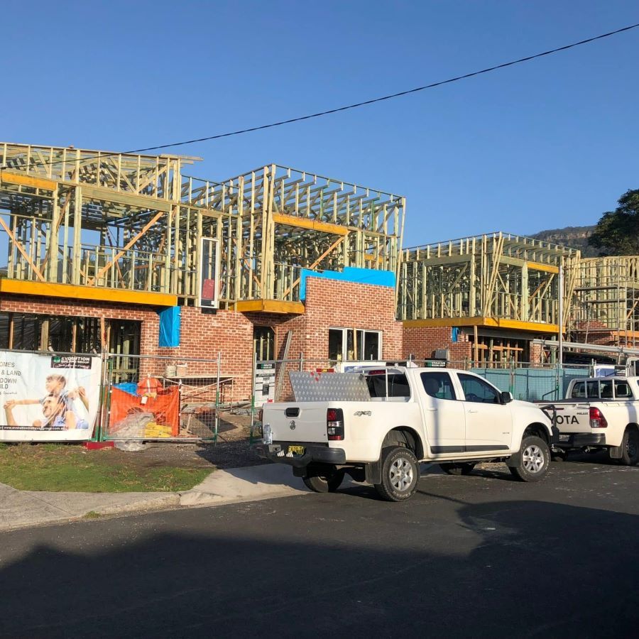 Two White Trucks Are Parked in Front of A Building Under Construction — Evolution Building Group Dapto, NSW