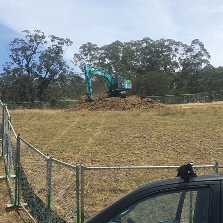 A Large Excavator Is Sitting on Top of A Pile of Dirt in A Field Behind a Fence — Evolution Building Group Dapto, NSW
