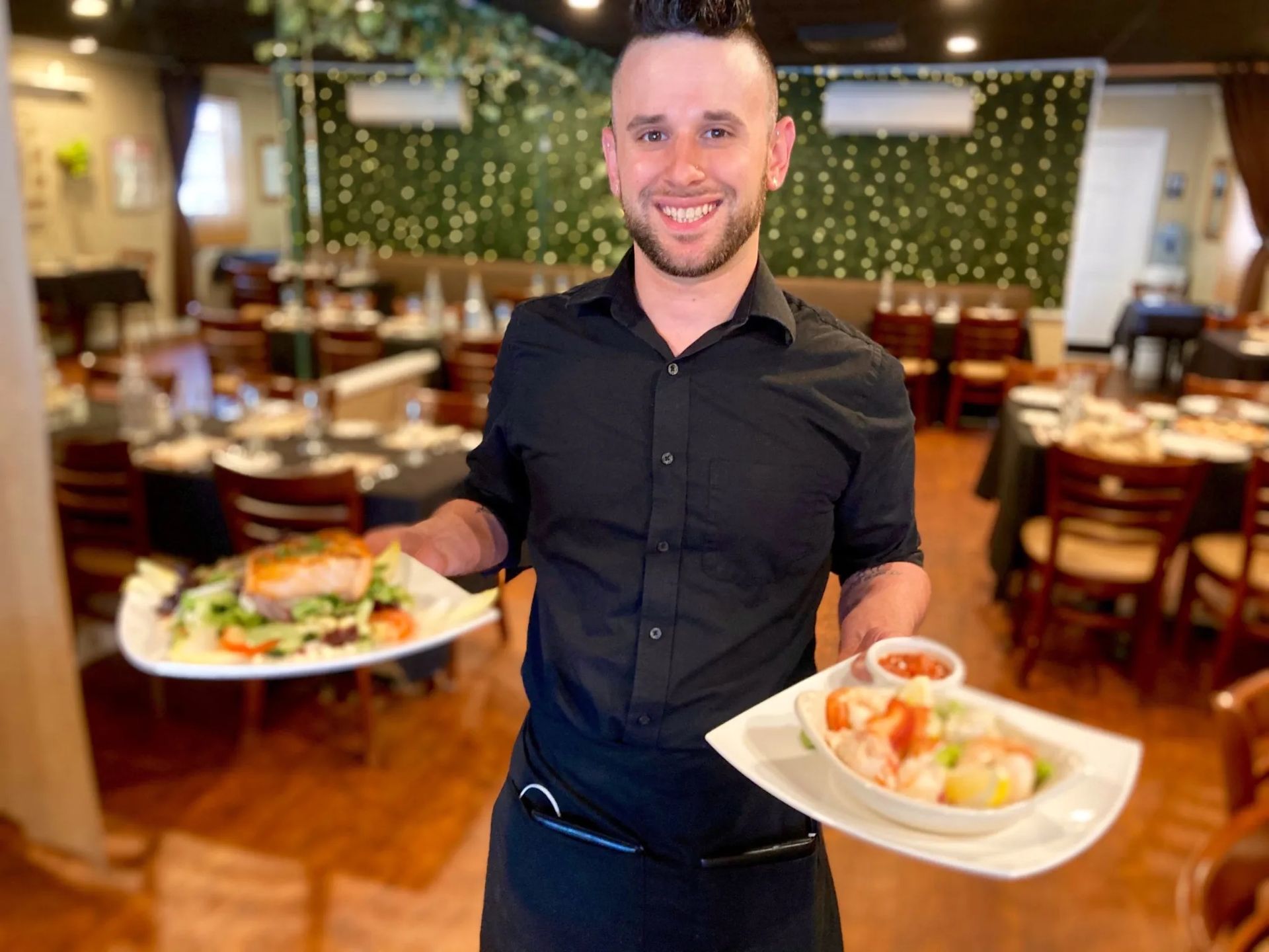 A waiter is holding two plates of food in a restaurant.