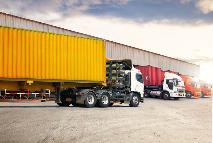 A row of semi trucks parked in front of a warehouse.