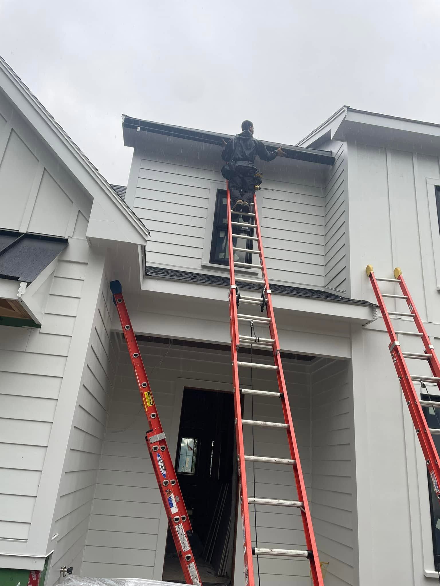 Worker on roof using ladders to inspect or repair a house exterior.