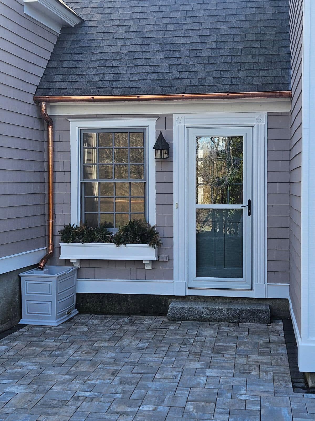 Small front entrance with white door, window, wall lantern, planter, and stone paver patio.