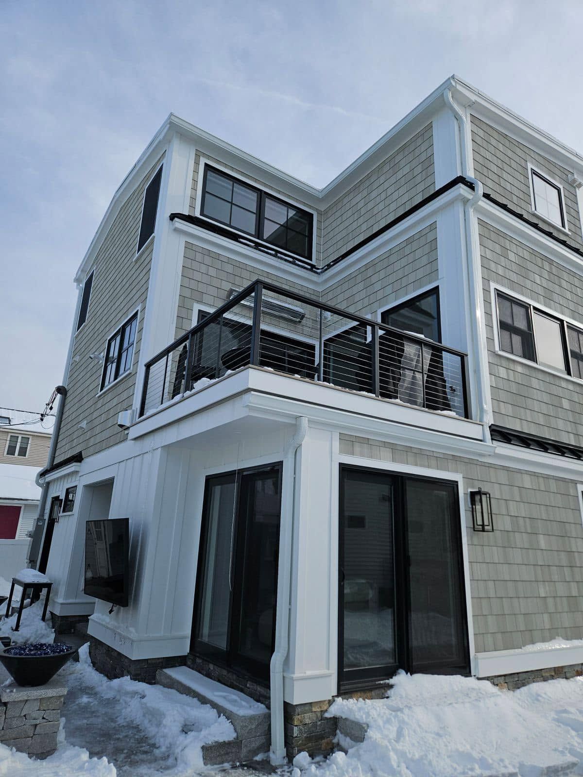 Modern three-story townhouse with gray siding, black balconies, and snow on the ground