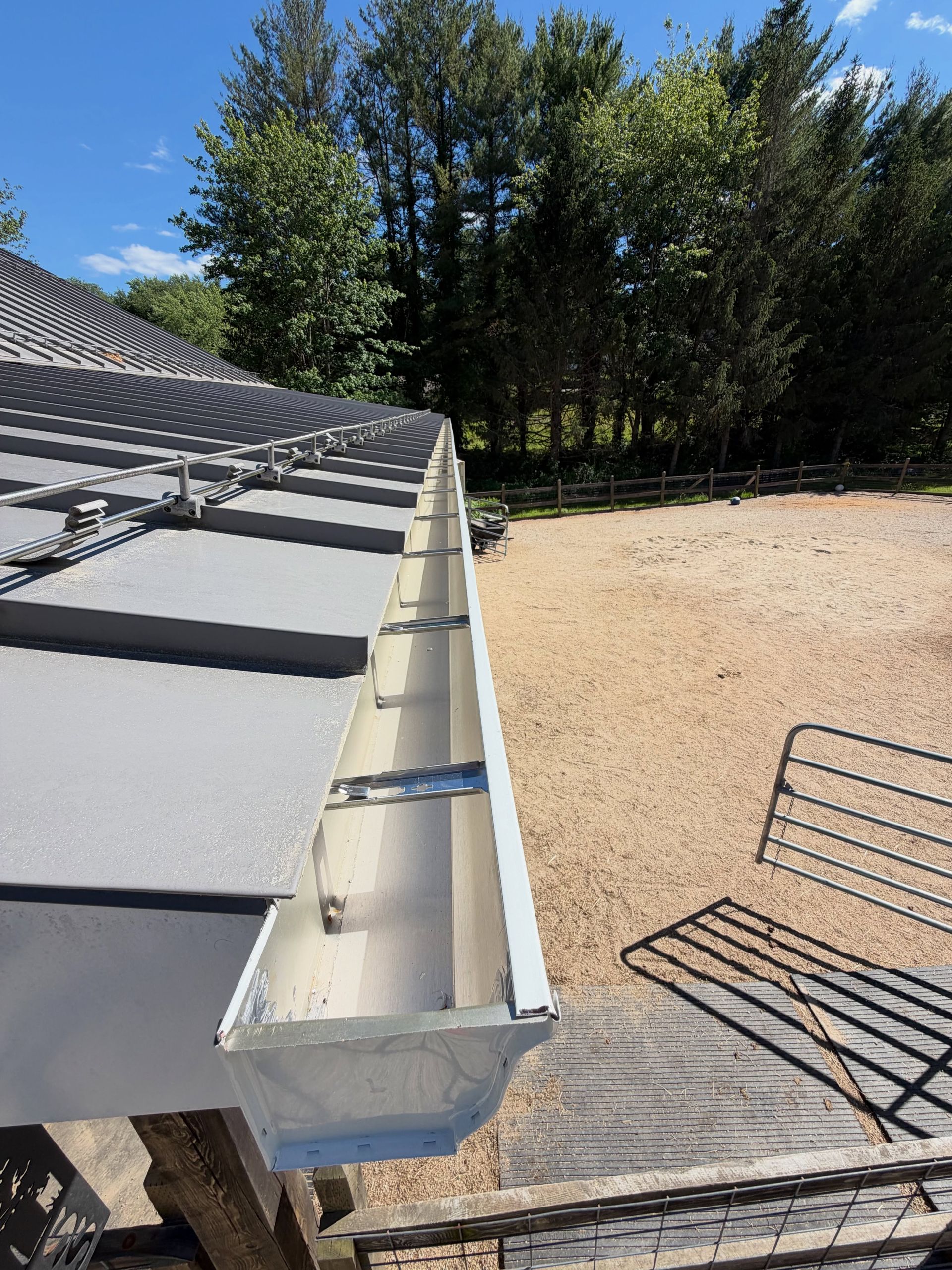 Gutter and roof edge beside a gravel yard with trees under a blue sky