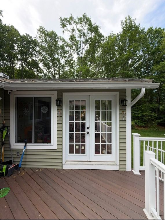 White French doors on a small house deck with railing and trees in the background