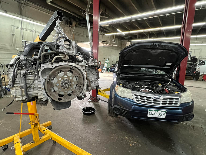 A car engine is being removed from a subaru forester in a garage. | Ridgeline Automotive