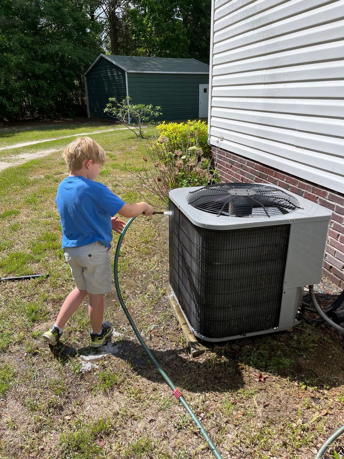A young boy is cleaning an air conditioner with a hose.