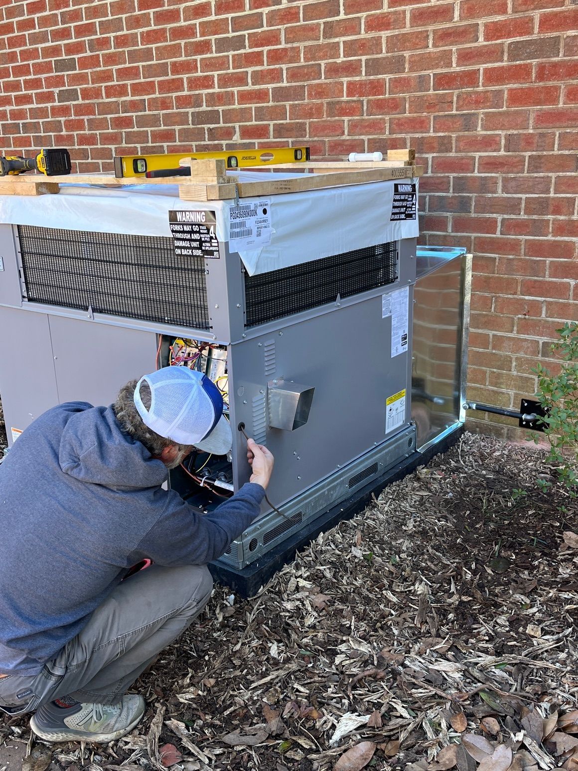 A man is working on an air conditioner outside of a brick building.