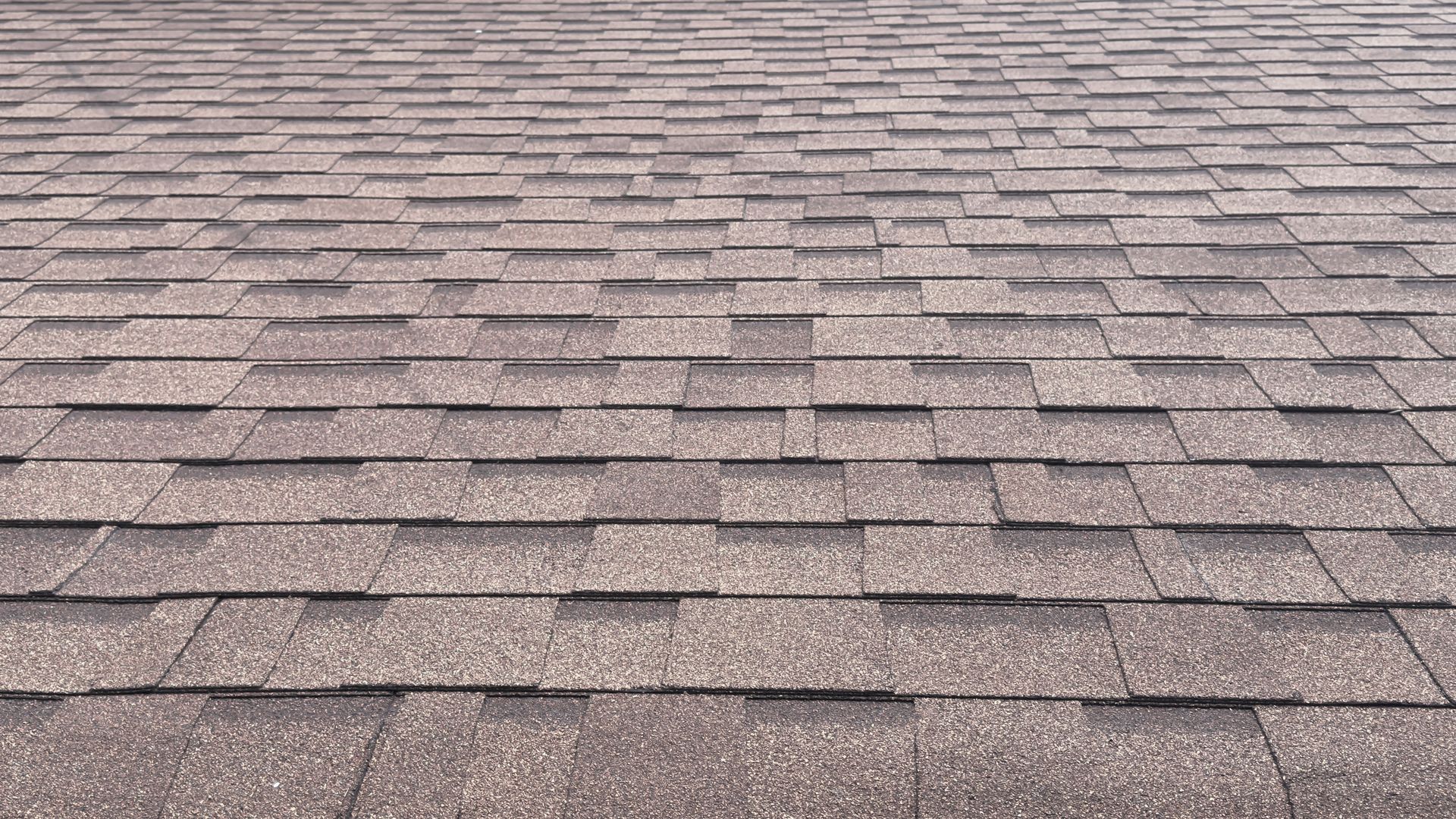 Brown asphalt shingle roof, with a layered pattern, viewed from a close-up perspective.