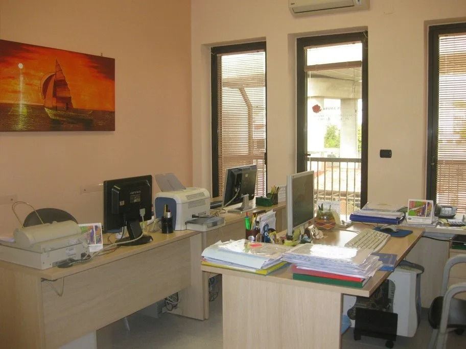 Office with two desks, computers, printer, and a painting of a sailboat. Two windows overlook a balcony.