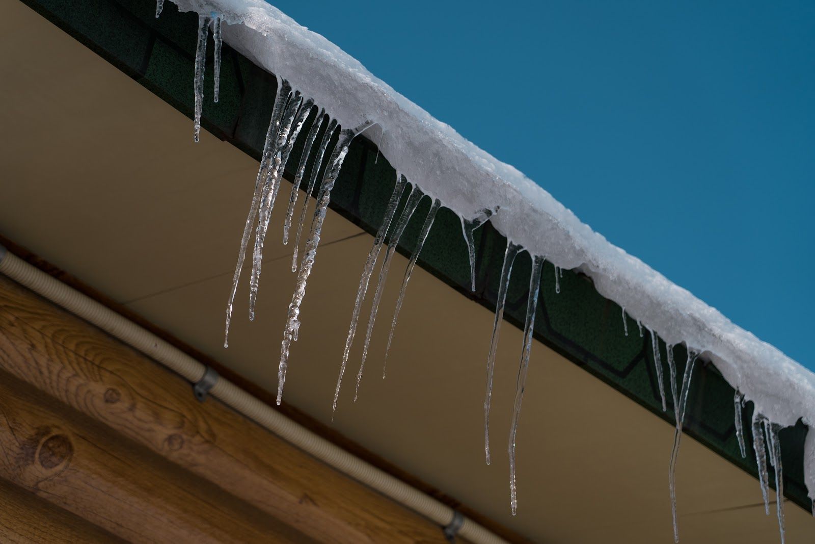 Icicles hanging from a snow-covered roof edge against a blue sky