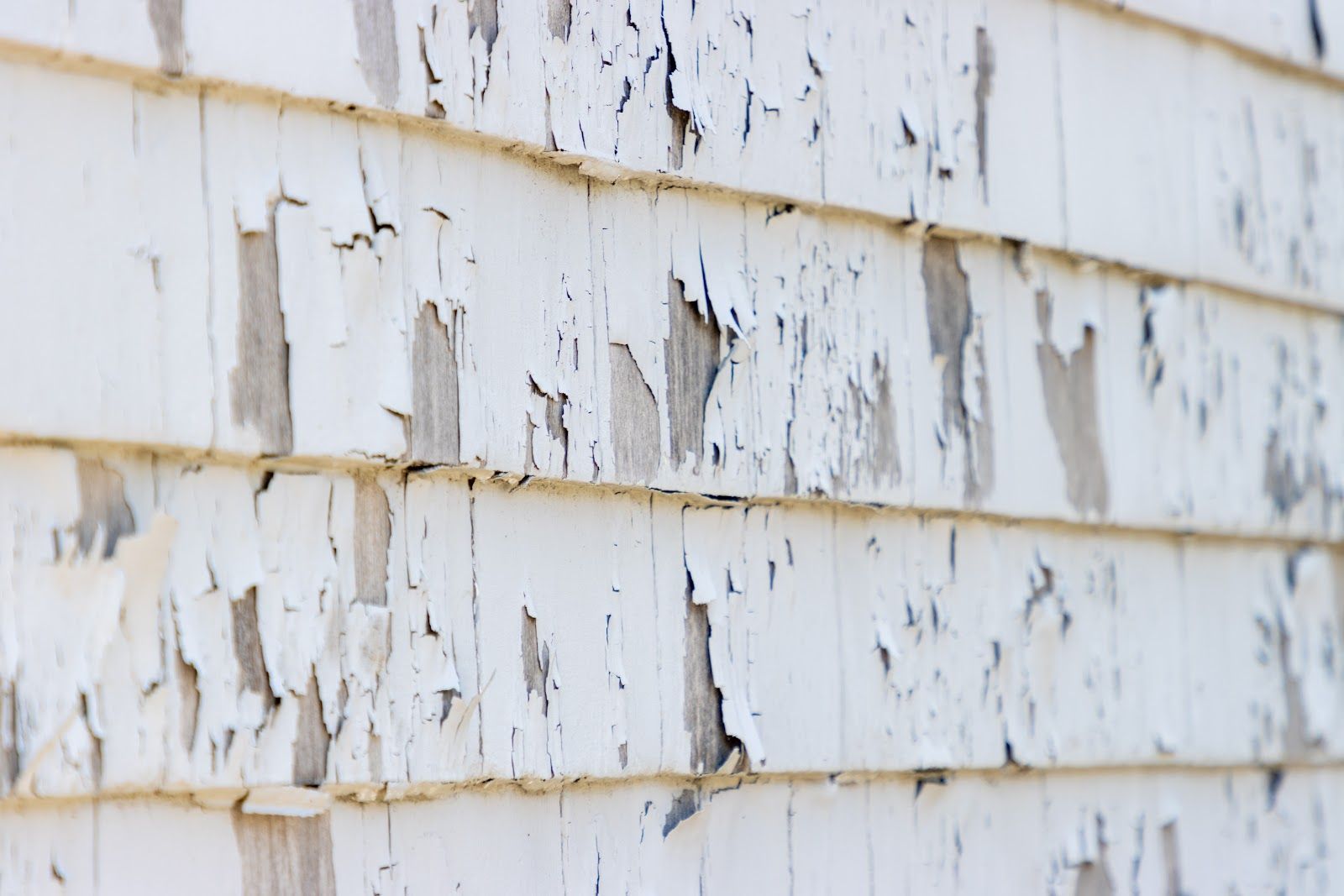 Peeling white paint on a weathered wooden wall with rust stains