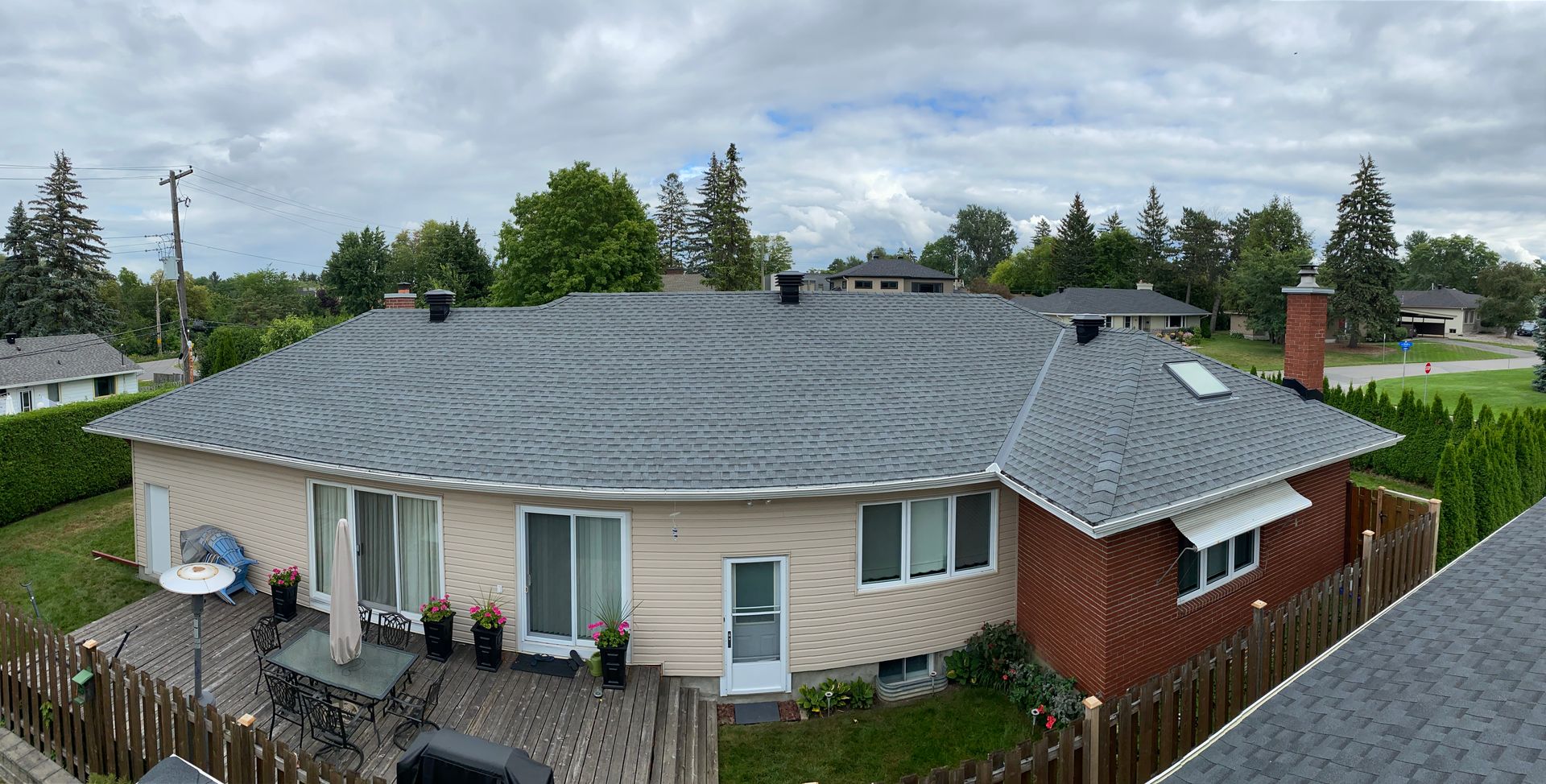 Single-story beige house with gray roof, red side siding, deck, and fenced yard under cloudy sky