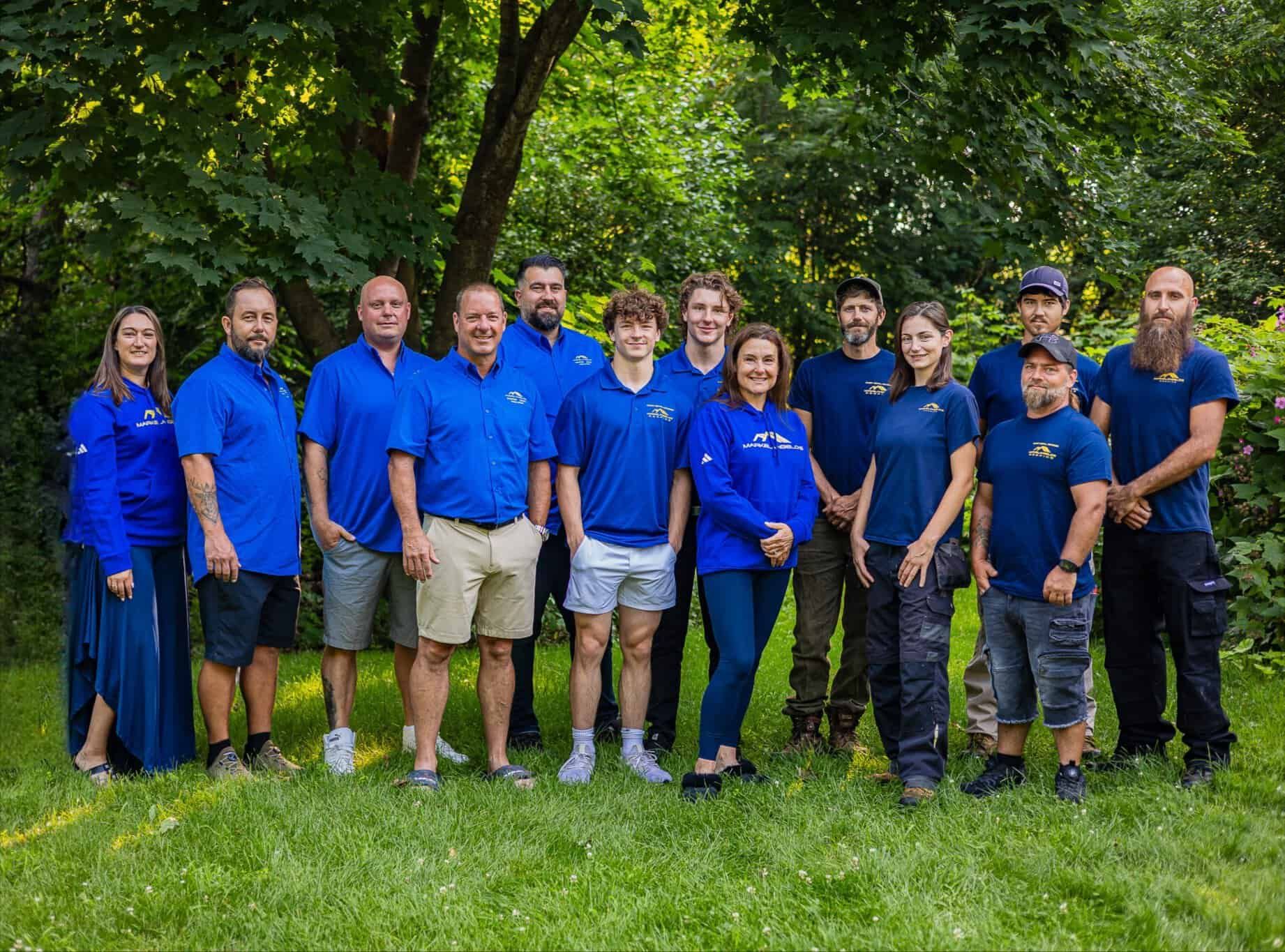 Group of people in blue shirts posing for a photo outdoors on a grassy lawn.