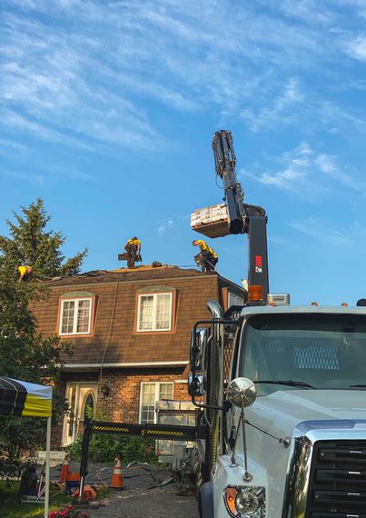 Roofers on a house with a boom lift delivering roofing materials under a blue sky.
