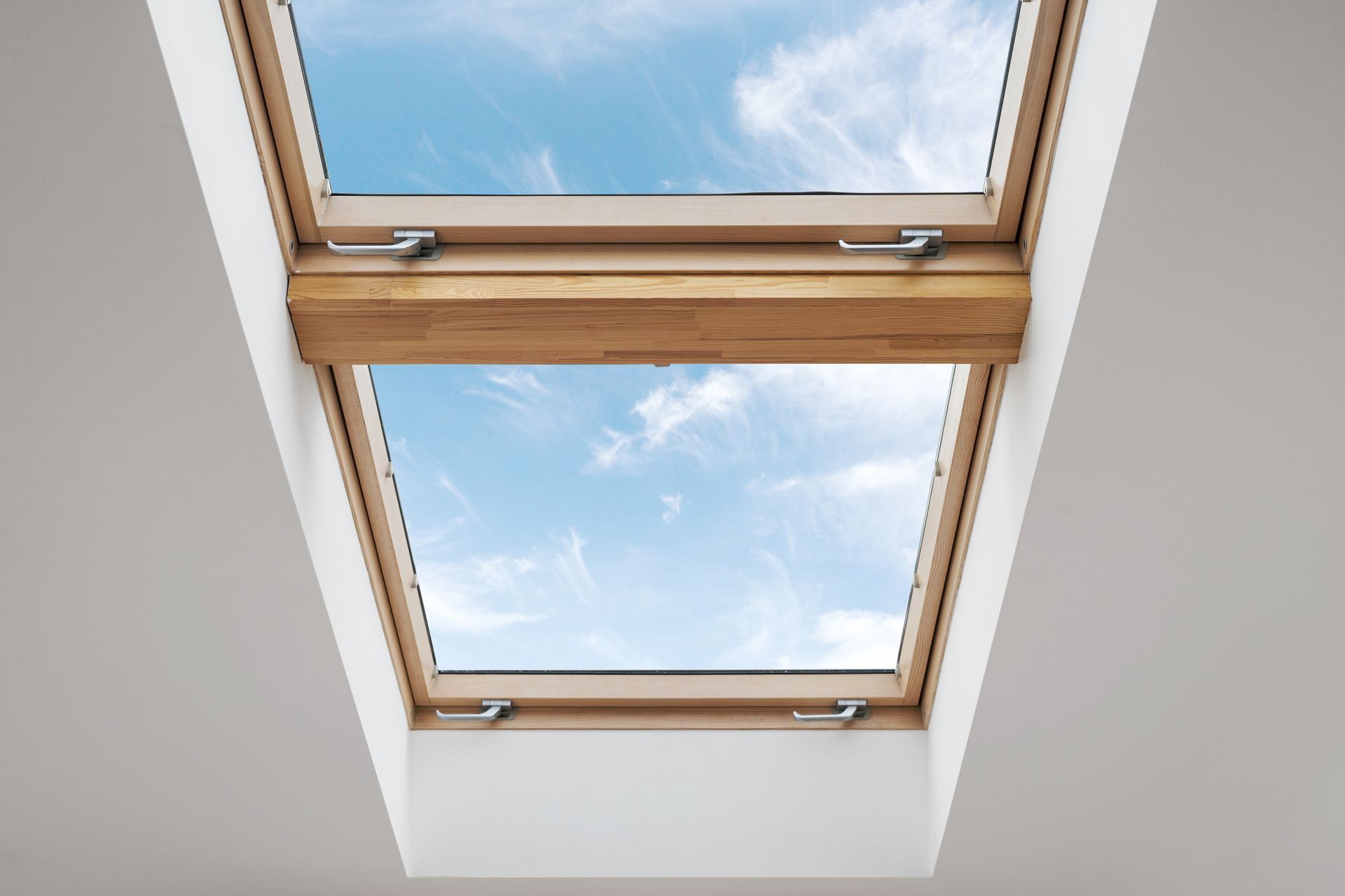Skylight with wooden frame open to blue sky and clouds.