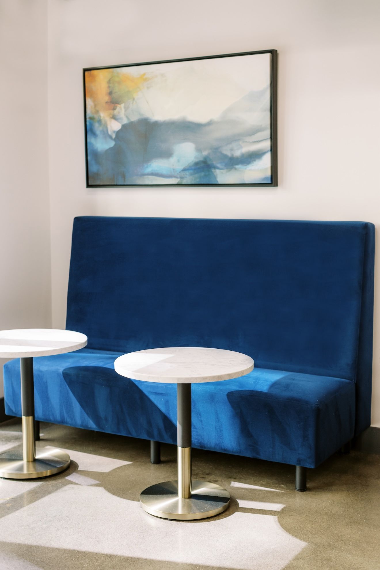 A blue couch and two tables in a room with a painting on the wall.