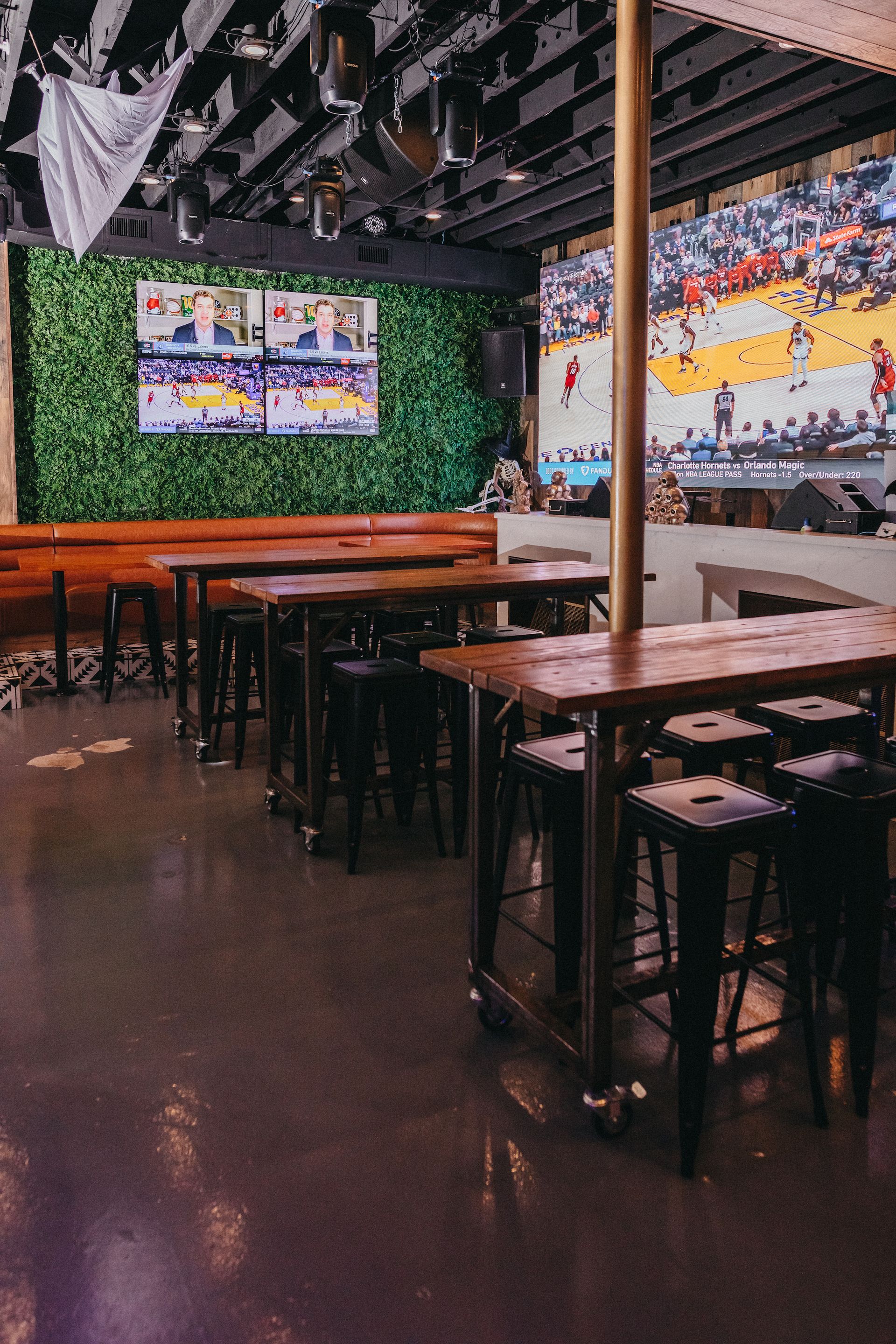 A restaurant with tables and stools and tv screens on the wall.