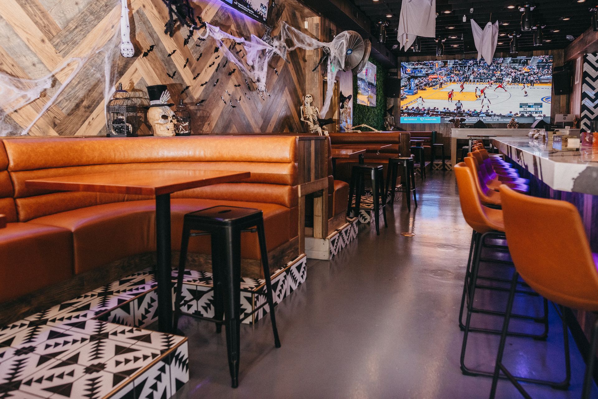 A restaurant with tables and chairs and a large screen on the wall.