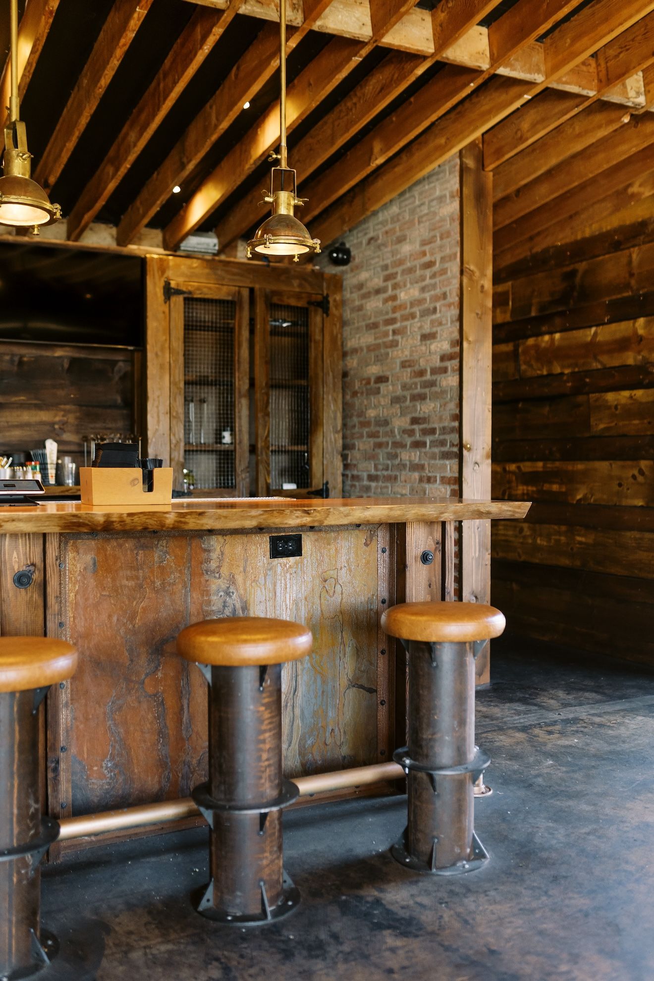 A wooden bar with stools in a room with a brick wall.