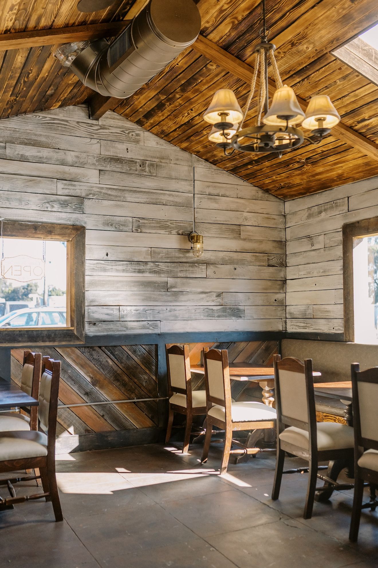 A restaurant with wooden tables and chairs and a chandelier.