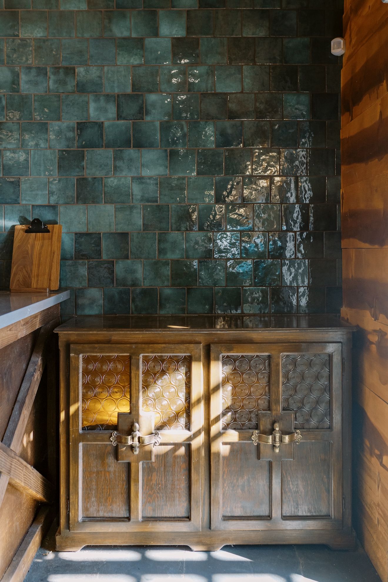 A wooden cabinet is sitting in front of a green tiled wall.