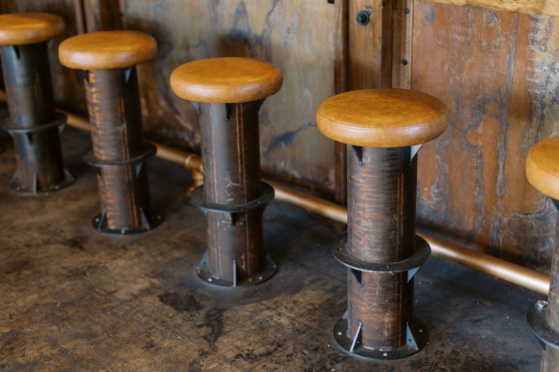 A row of wooden bar stools sitting next to each other on a concrete floor.