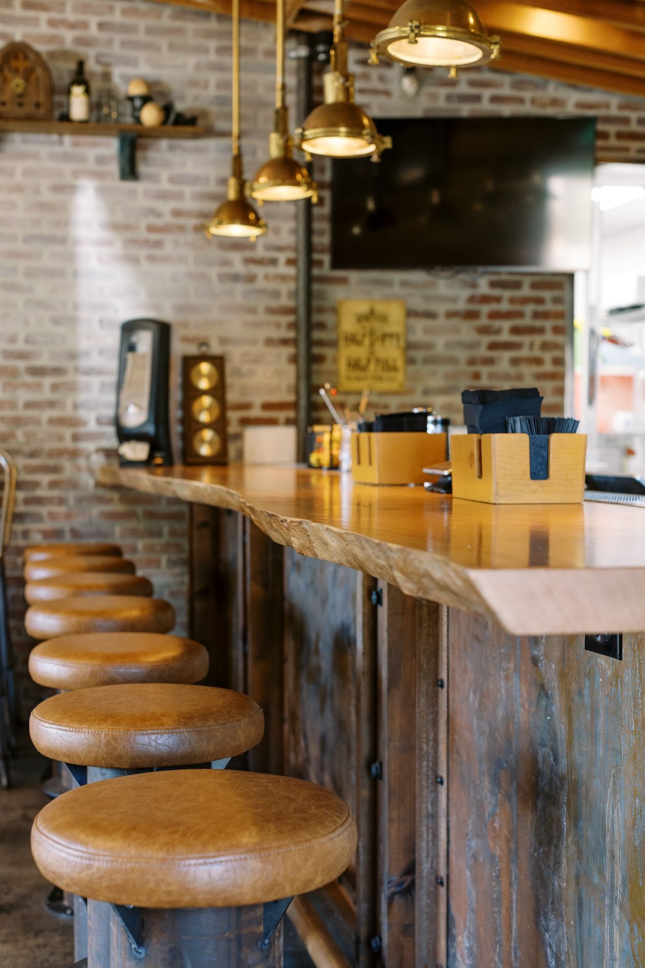 A long wooden bar with stools in a restaurant with a brick wall.