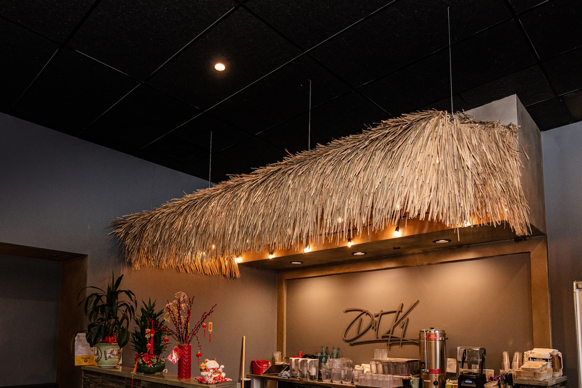A thatched roof is hanging from the ceiling of a restaurant.