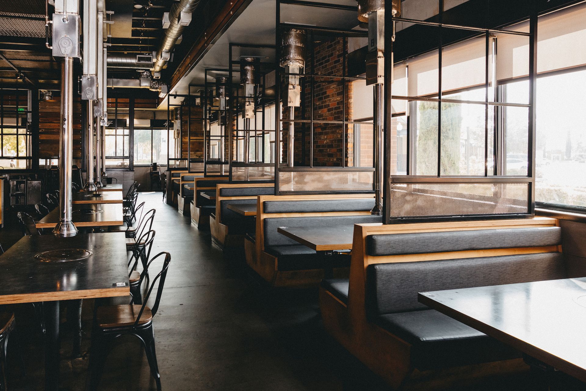 A restaurant with tables and benches and lots of windows.