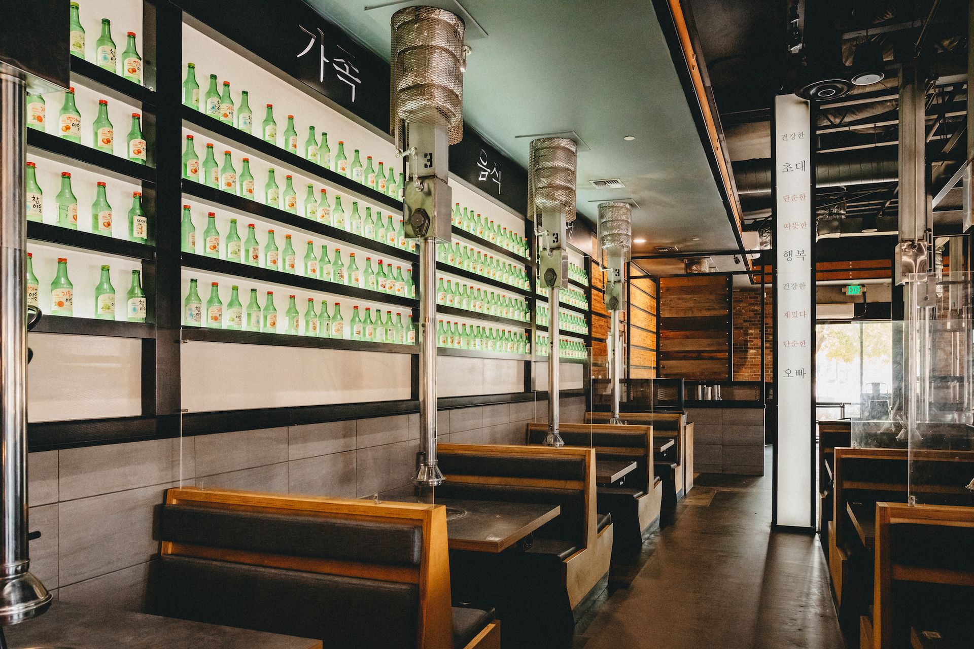 A restaurant with tables and benches and bottles on the wall.
