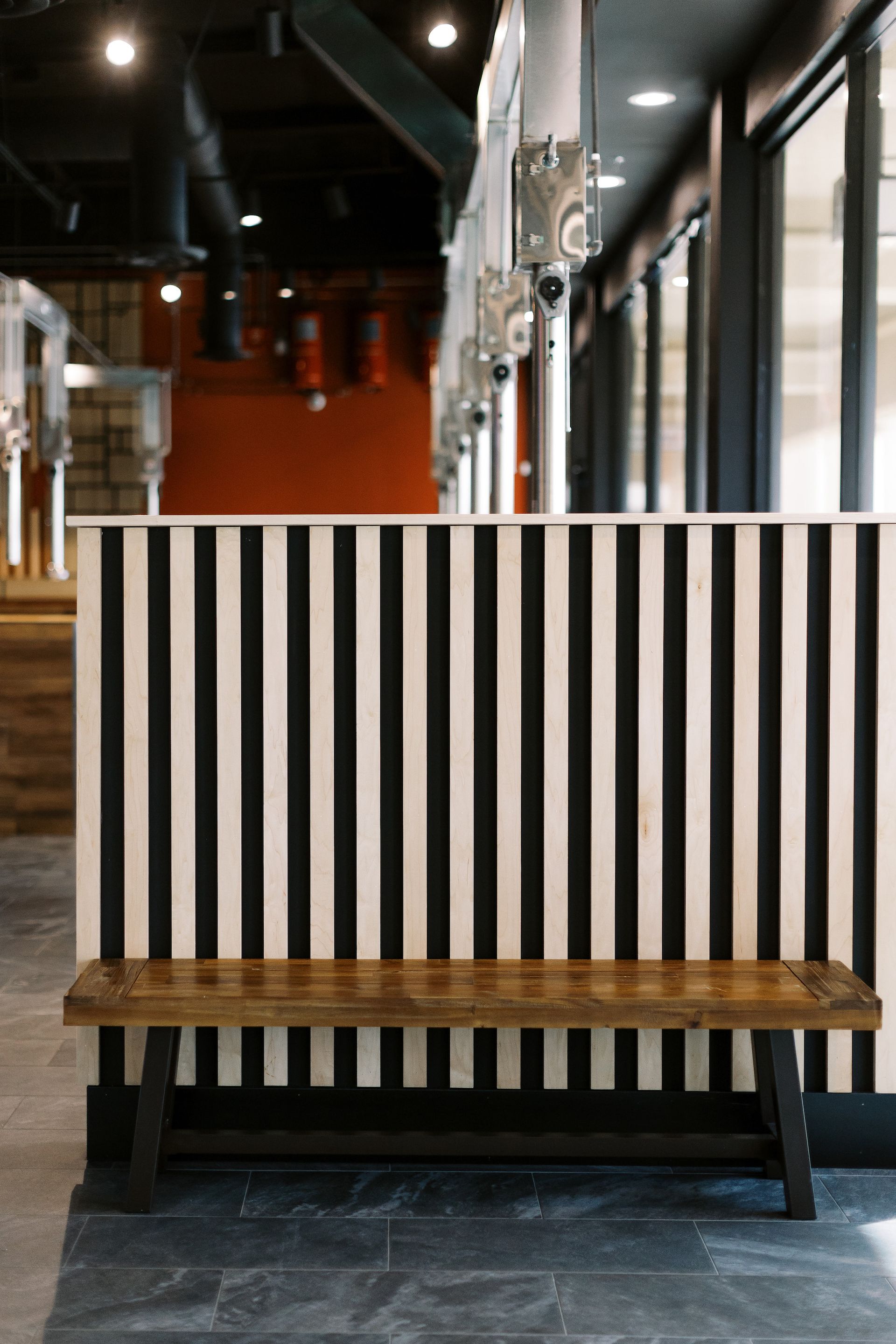 A wooden bench is sitting in front of a black and white striped wall.