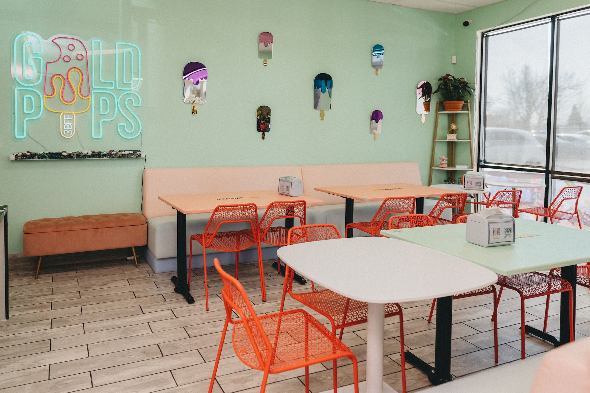 A restaurant with tables and chairs and a neon sign that says cold pops.