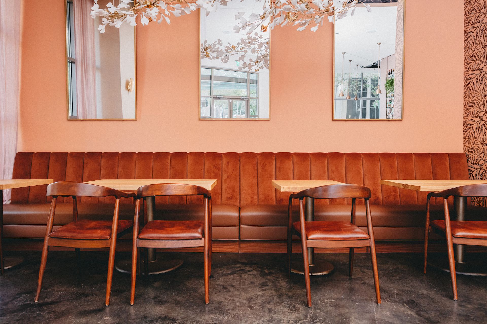A row of tables and chairs in a restaurant with a pink wall.