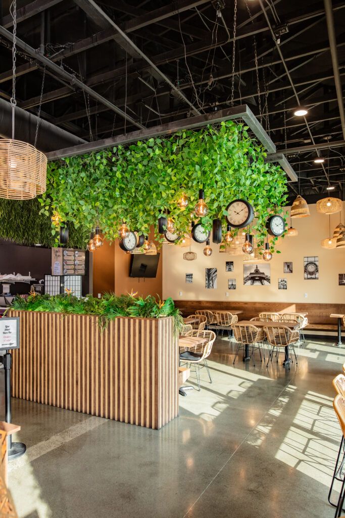 A restaurant with a ceiling covered in greenery and clocks hanging from it.