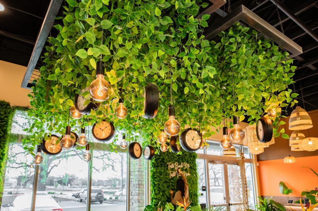 A restaurant with a ceiling covered in greenery and lights hanging from it.