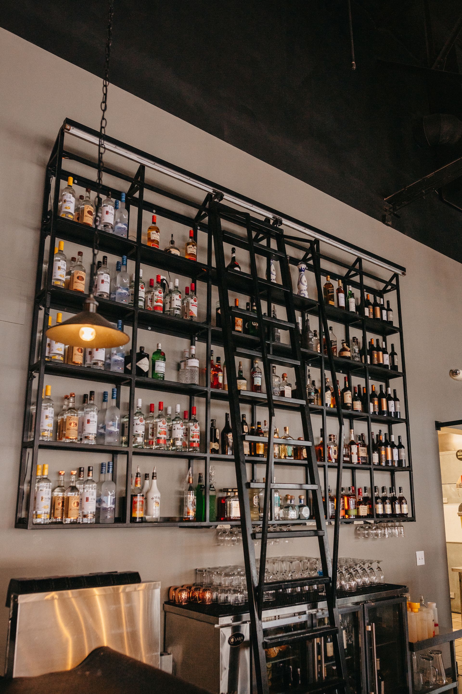 A bar with a ladder and lots of bottles on the shelves.