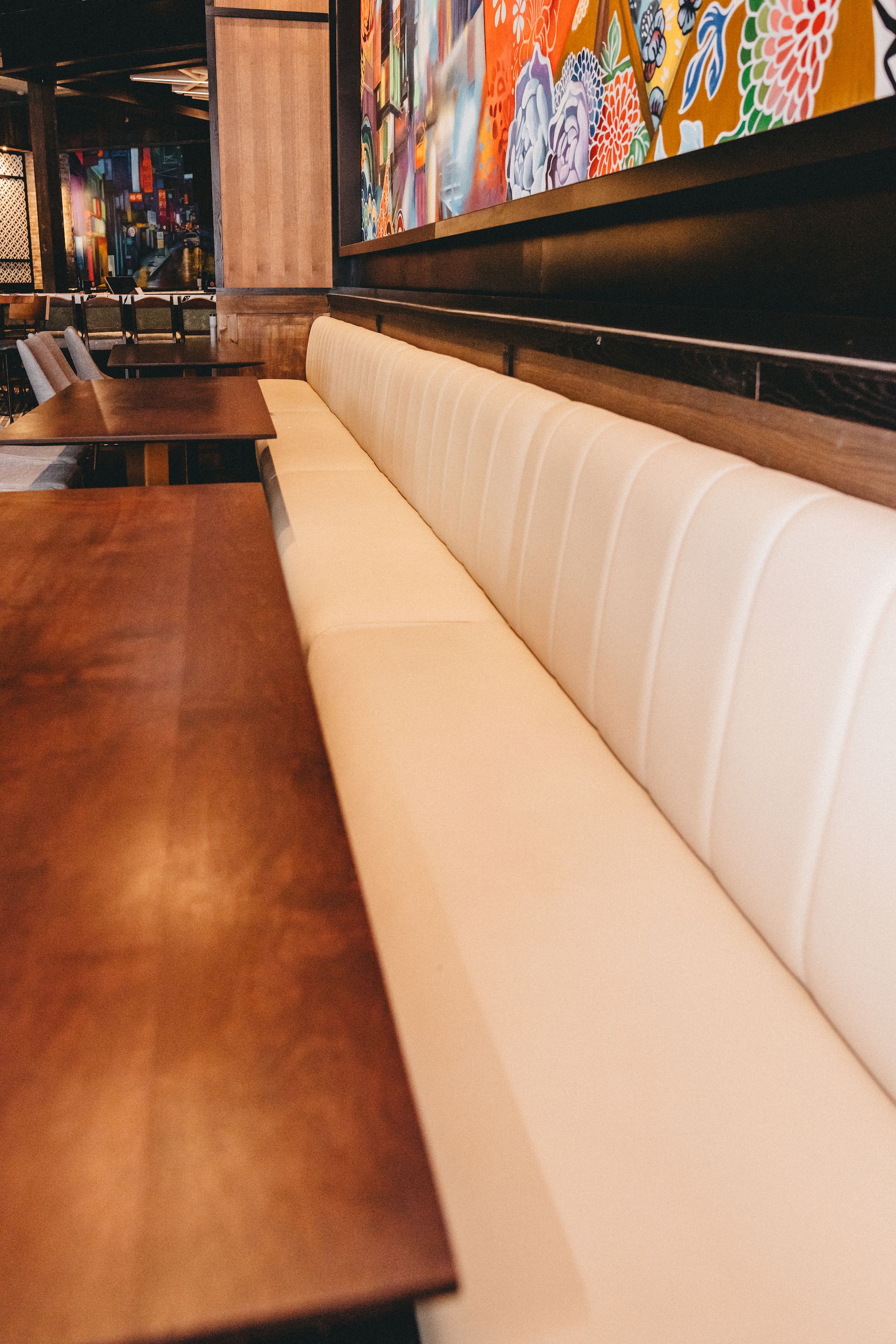 A row of tables and benches in a restaurant with a painting on the wall behind them.