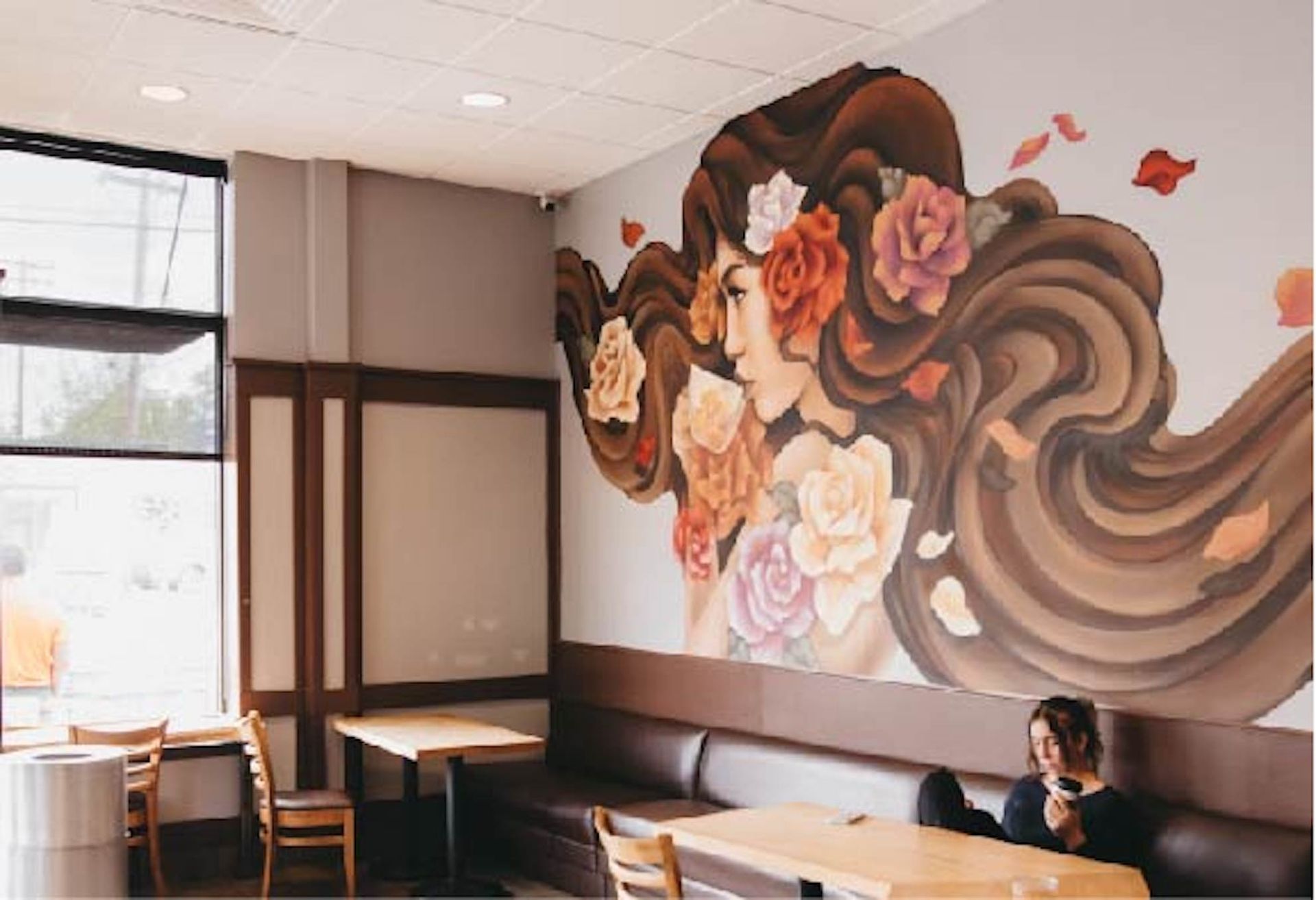 A woman is sitting at a table in a coffee shop with a mural on the wall.
