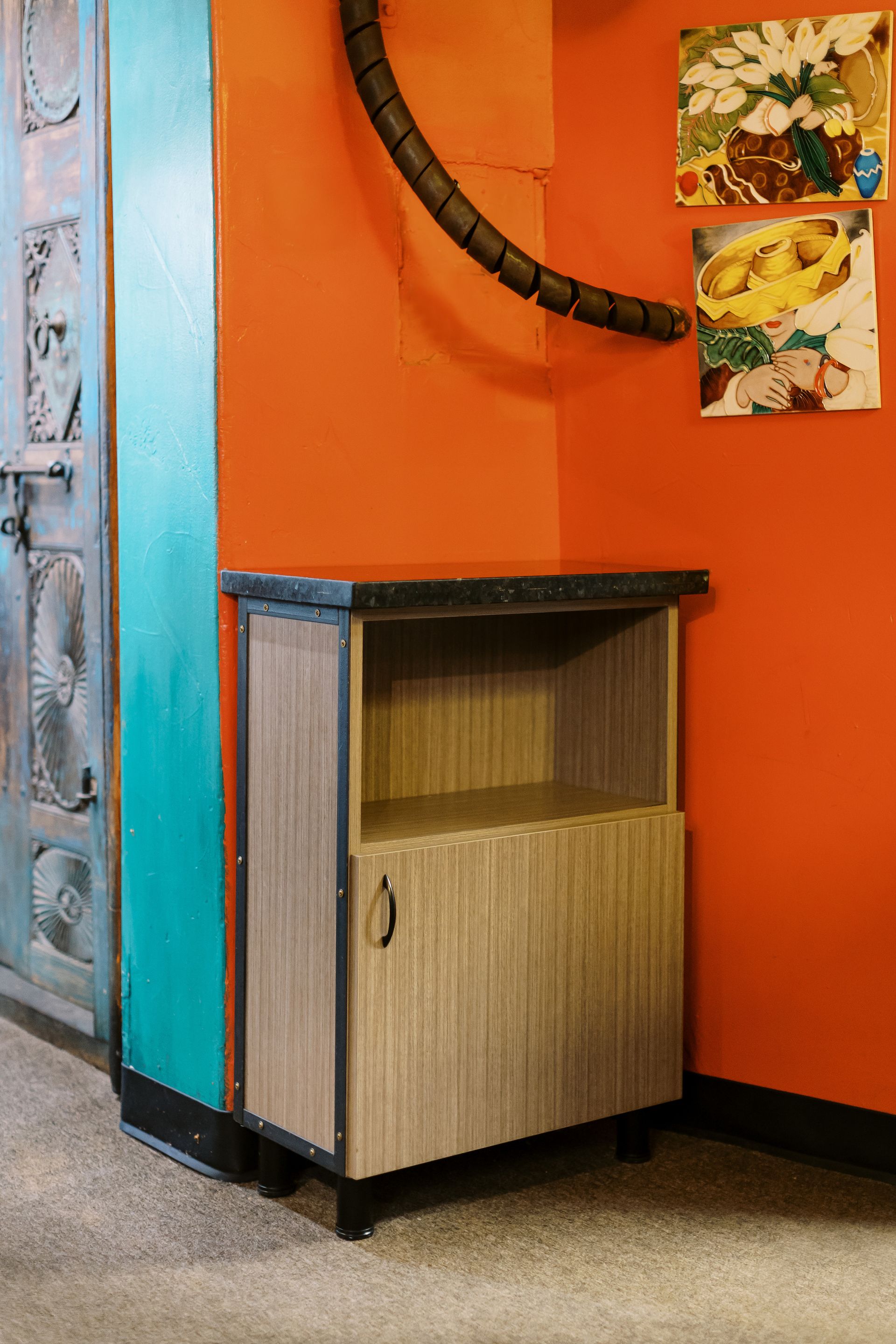 A small wooden cabinet is sitting in a corner of a room next to an orange wall.