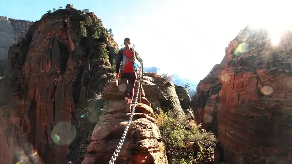Four hikers with large backpacks trek along a rugged, rocky ridge toward mountains under a hazy, golden sky.