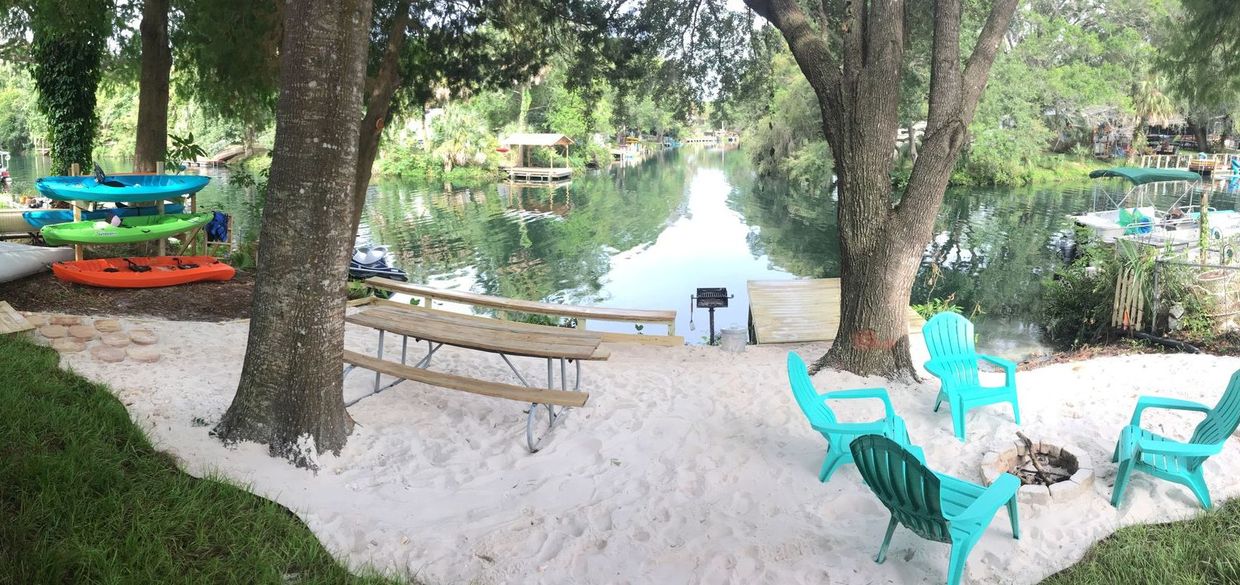 A picnic table and chairs are sitting in the sand near a river.