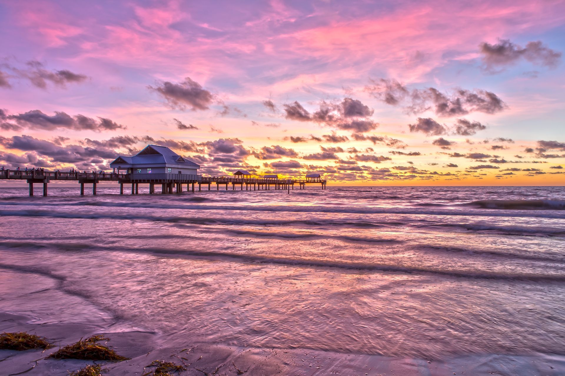 A pier on a beach at sunset with a purple sky