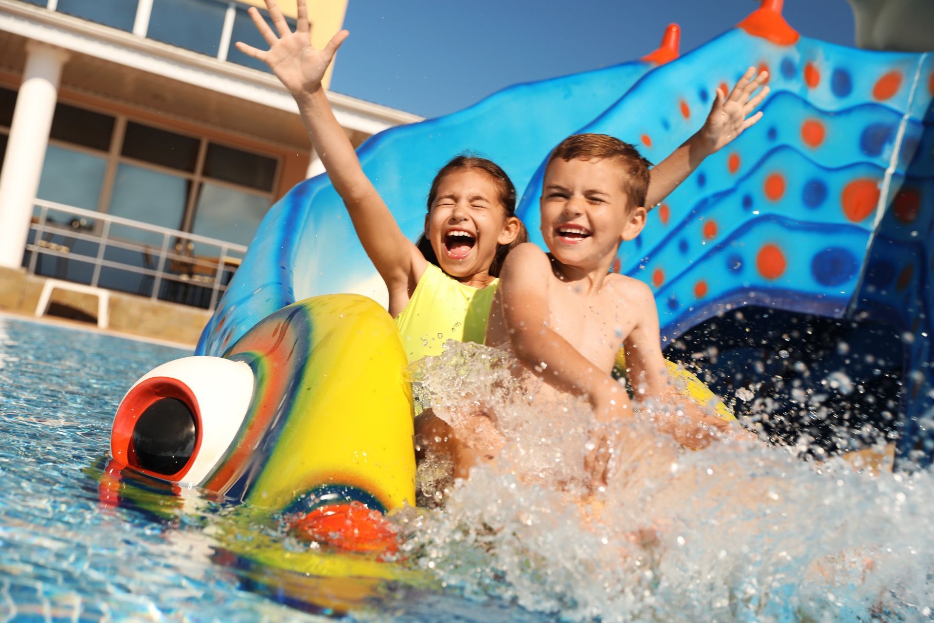 A boy and a girl are playing on a water slide in a swimming pool.