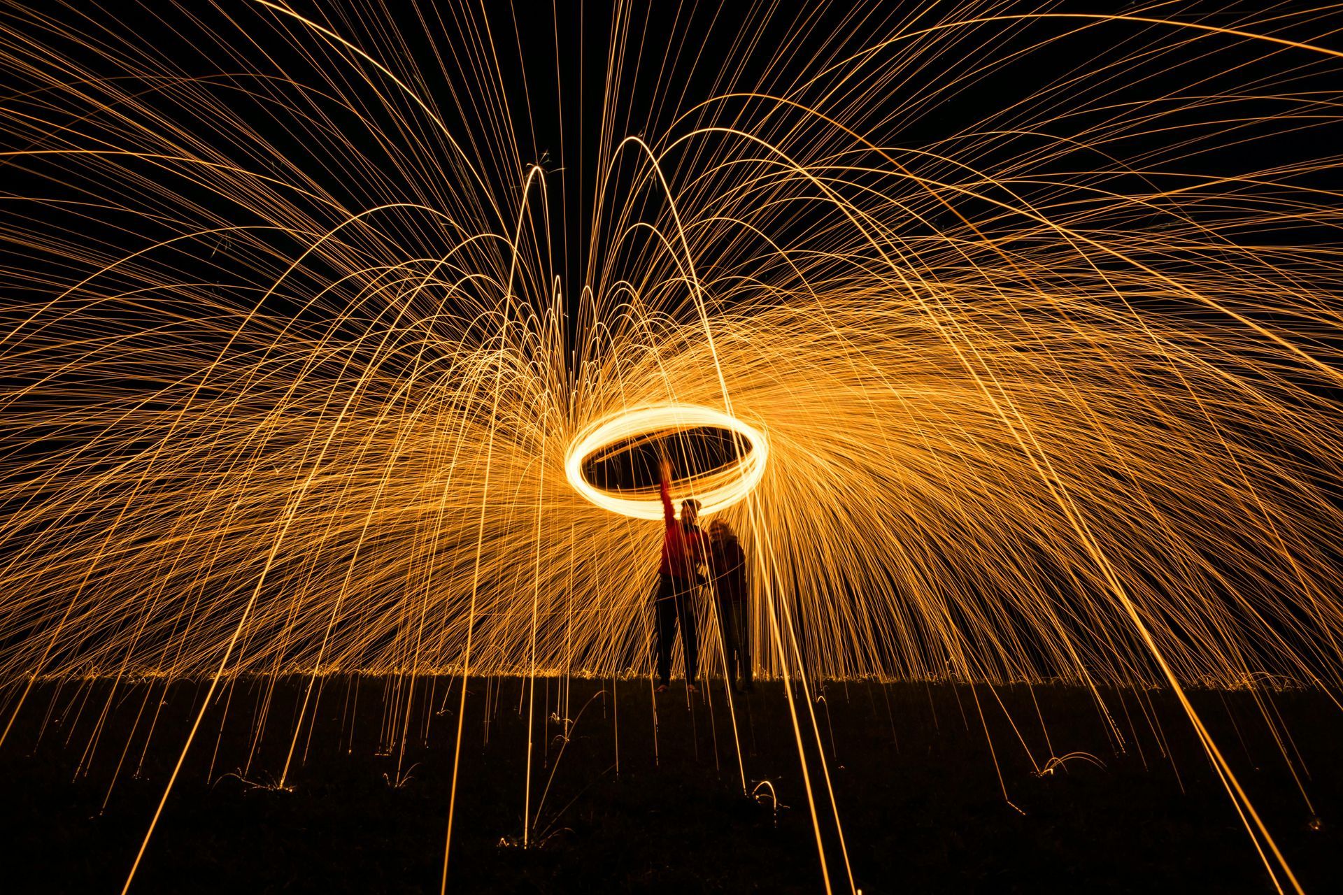 Person spinning fiery steel wool creating light trails in the dark.