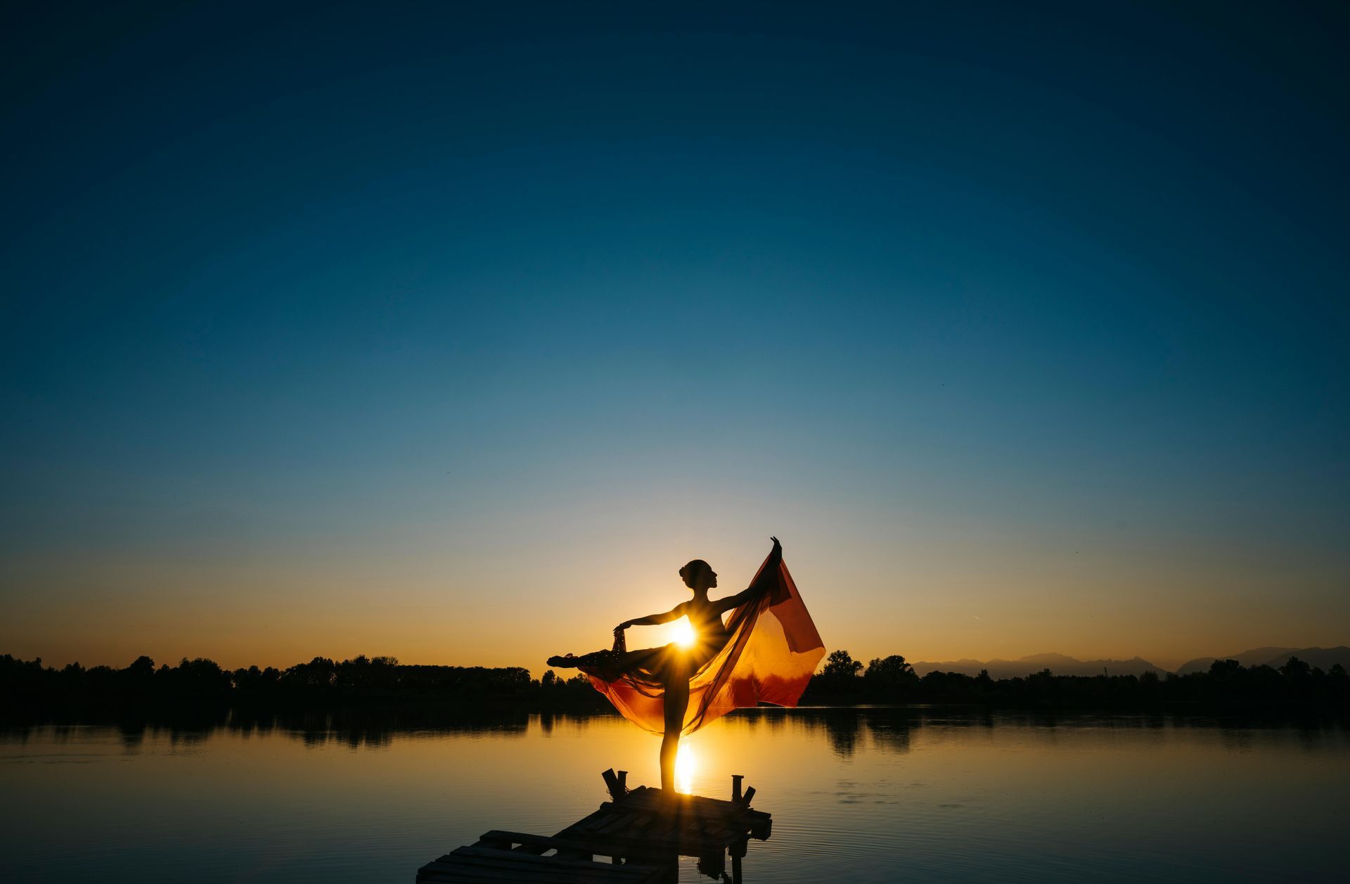 A person is standing on a raft in the water at sunset.