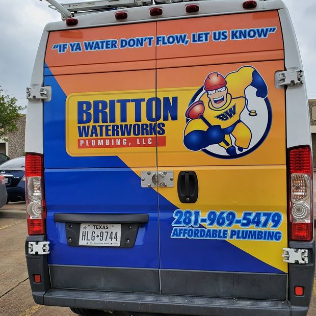 Rear view of a work van for Britton Waterworks, featuring a cartoon plumber mascot, contact info, and
