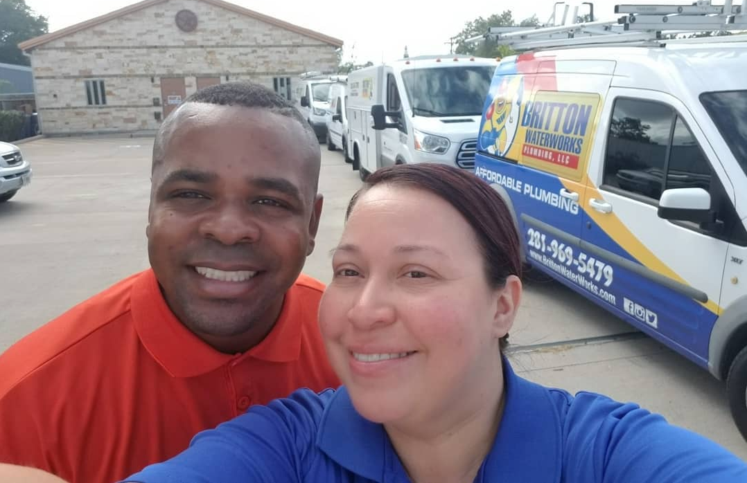 Two people smiling in front of Britton Plumbing and HVAC service vans parked in a lot.