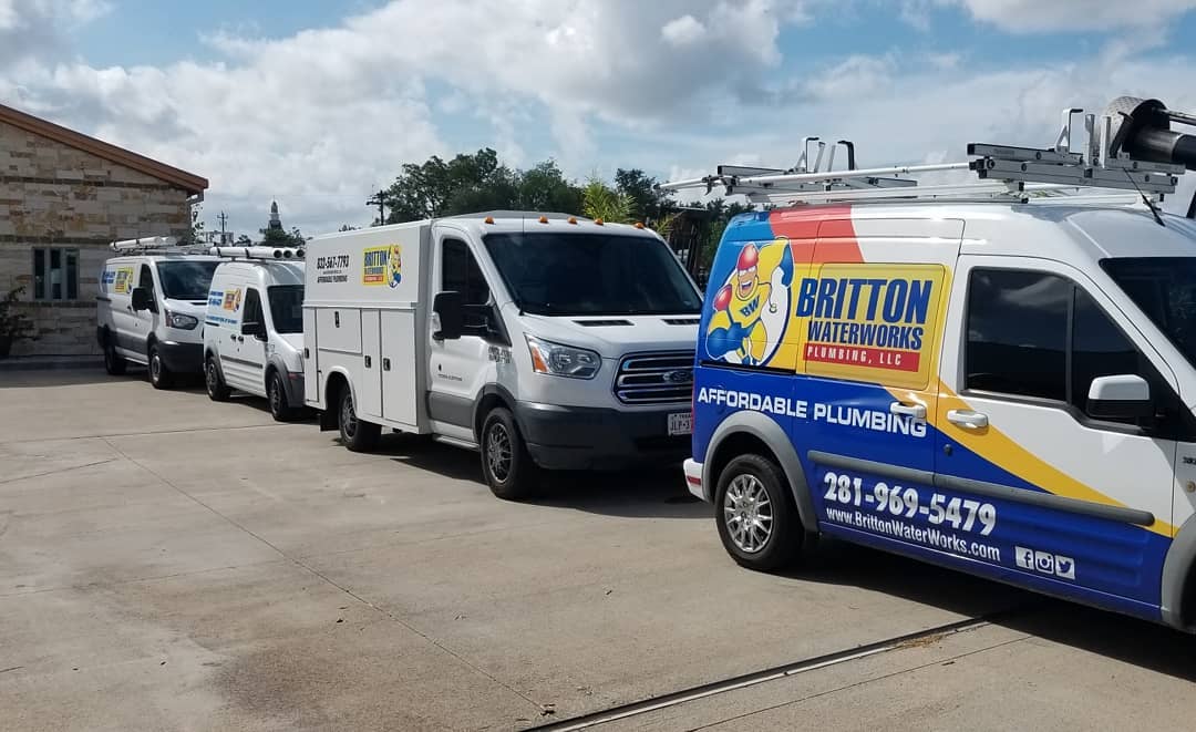 A line of service vans parked on a concrete lot, including a branded Britton Plumbing vehicle in the foreground.